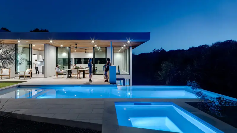 A pool and spa beside a glass-fronted house at dusk