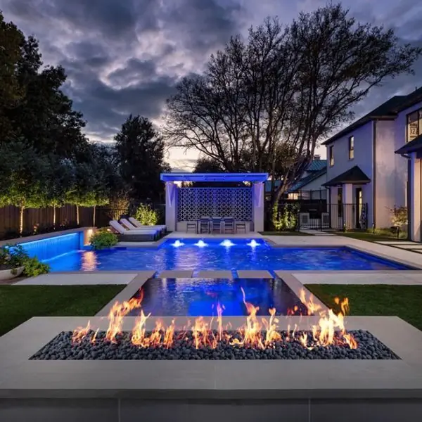 A pool with a fire pit and a lit pergola at dusk