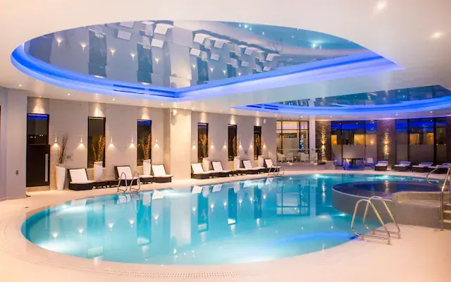 An indoor spa pool with loungers under a lit ceiling