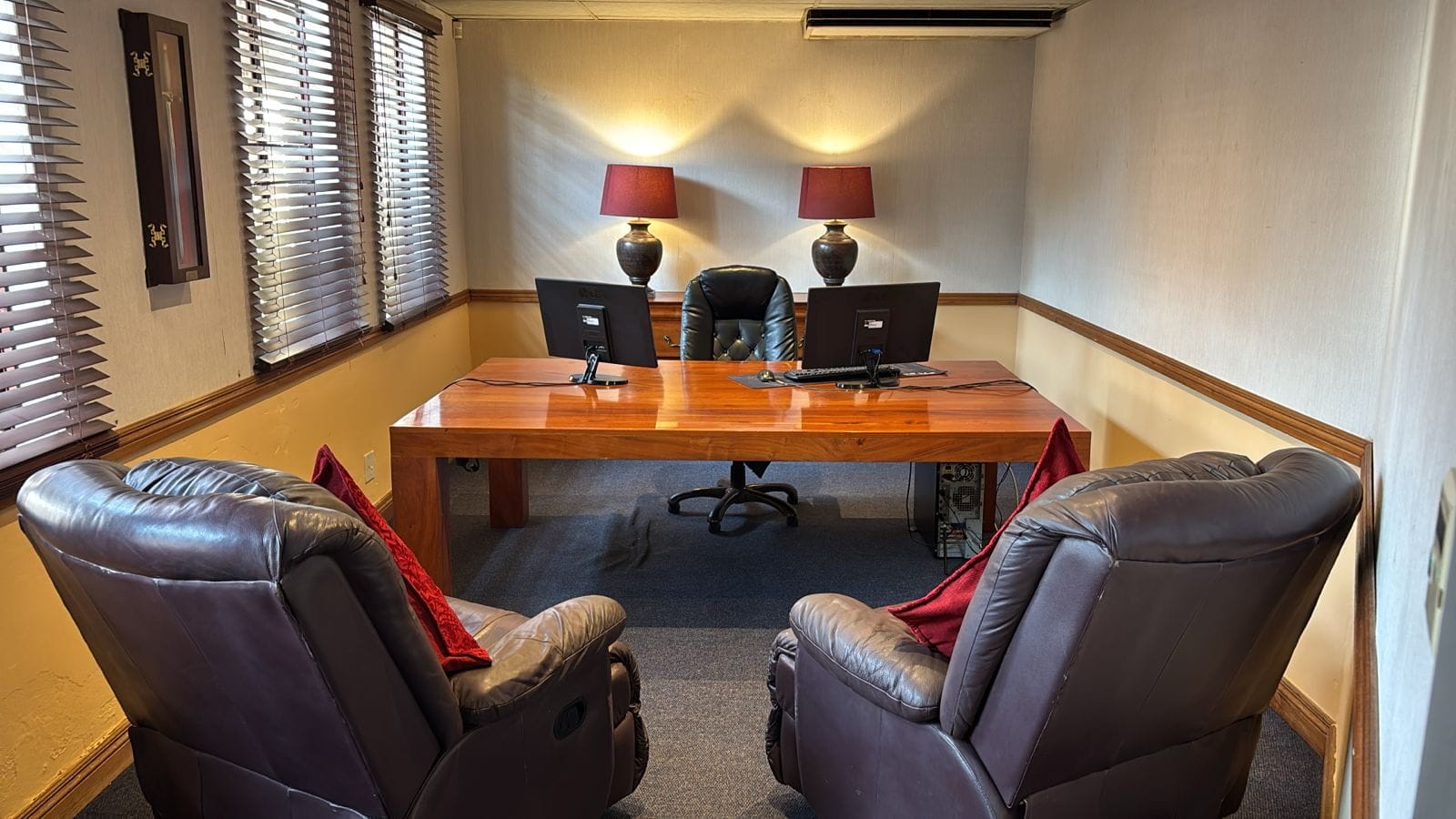 Private consultation office with a wooden desk, two monitors and leather armchairs