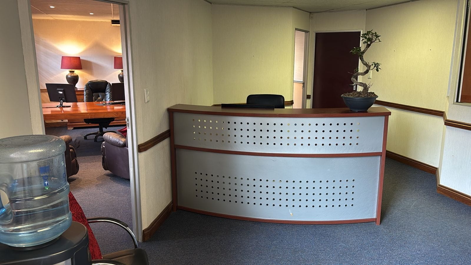Curved reception desk with a bonsai tree and a view into the consultation office